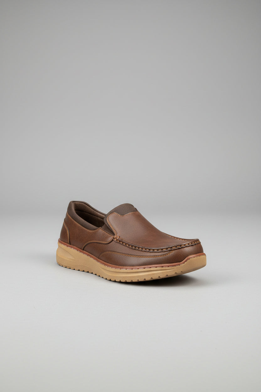 A brown suede slip-on loafer-style shoe with a thick tan sole, displayed on the arm of a green velvet sofa inside a shoe store.
